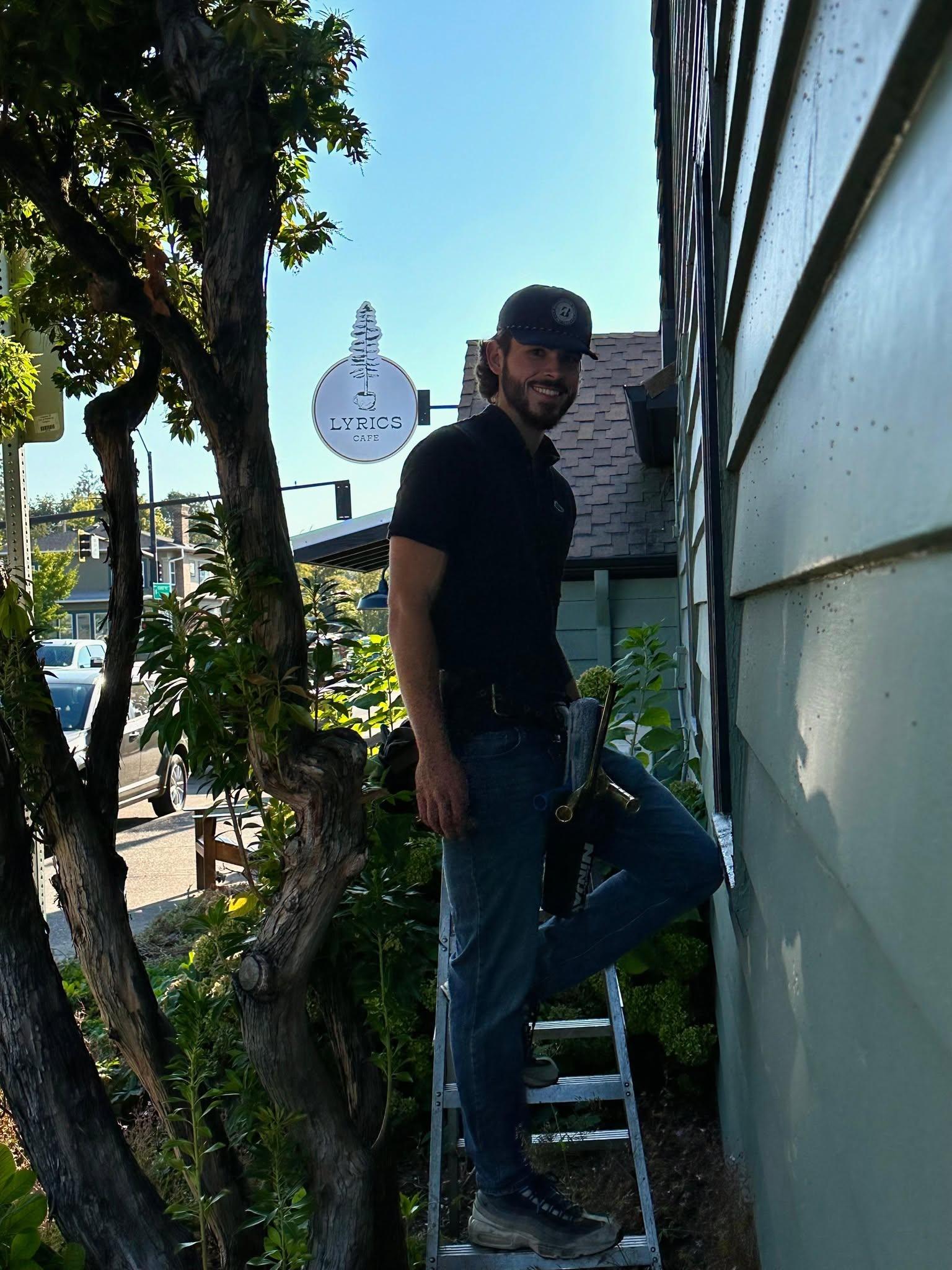 A friendly Valley Boys technician on a ladder at a storefront