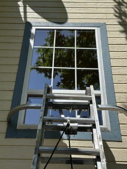 A Valley Boys technician cleaning a second-story window from a ladder
